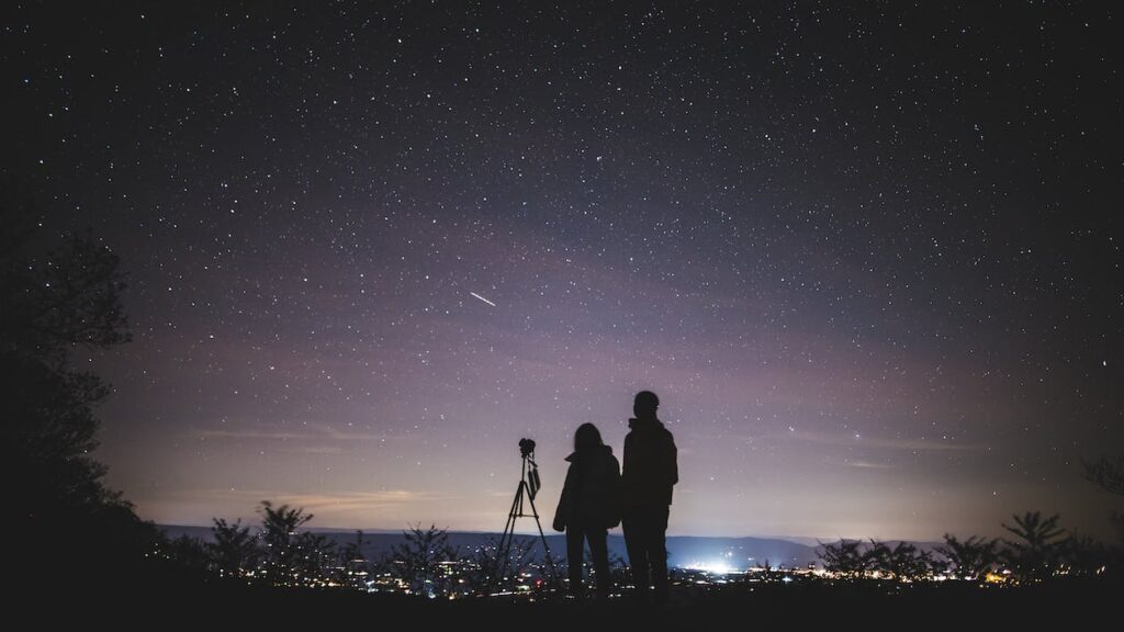 Silhouette de deux personnes debout observant le ciel dans la nuit. Photo : Licence Creative Commons