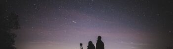 Silhouette de deux personnes debout observant le ciel dans la nuit. Photo : Licence Creative Commons